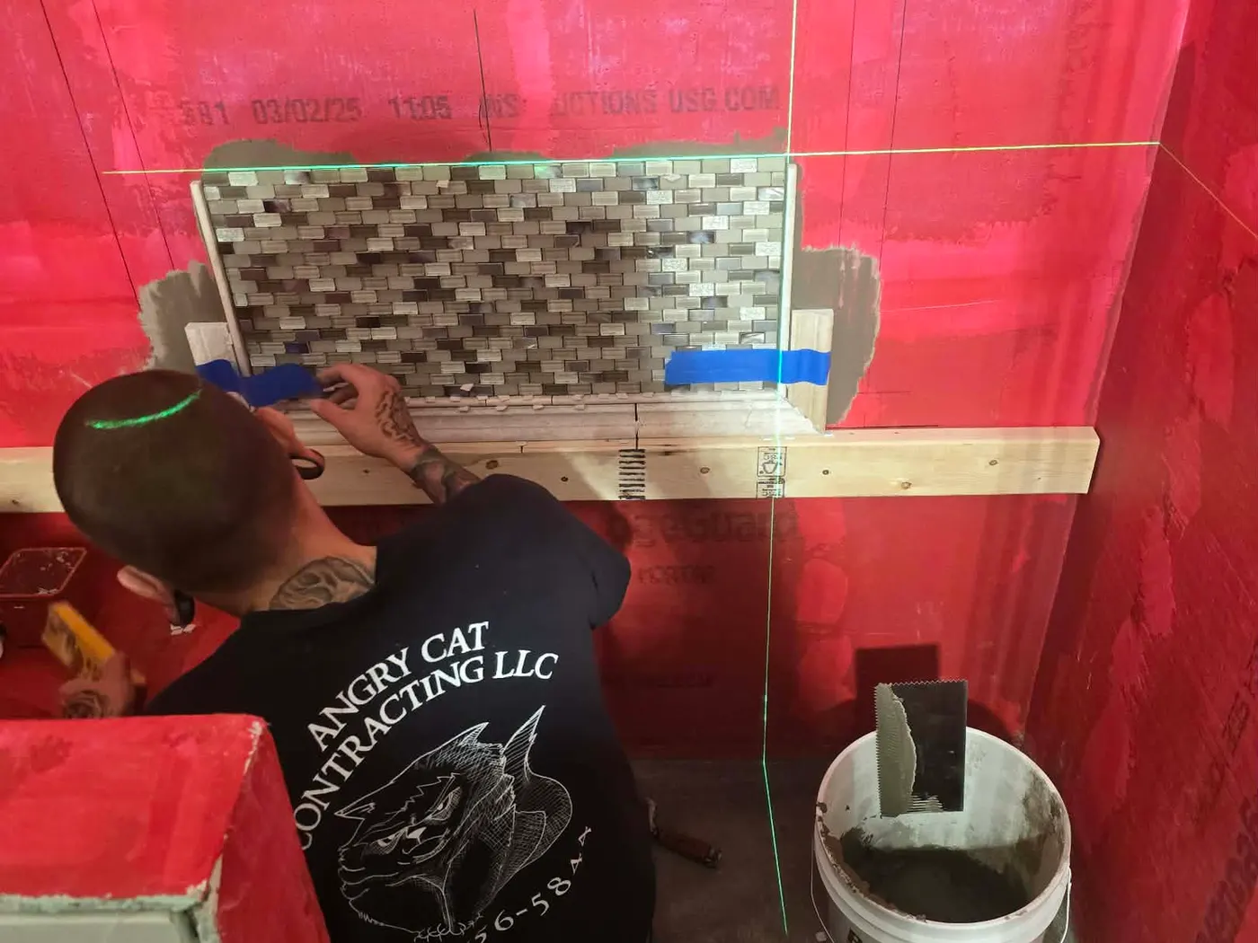 An Angry Cat Contracting owner in a company shirt setting mosaic tile over red waterproofing membrane