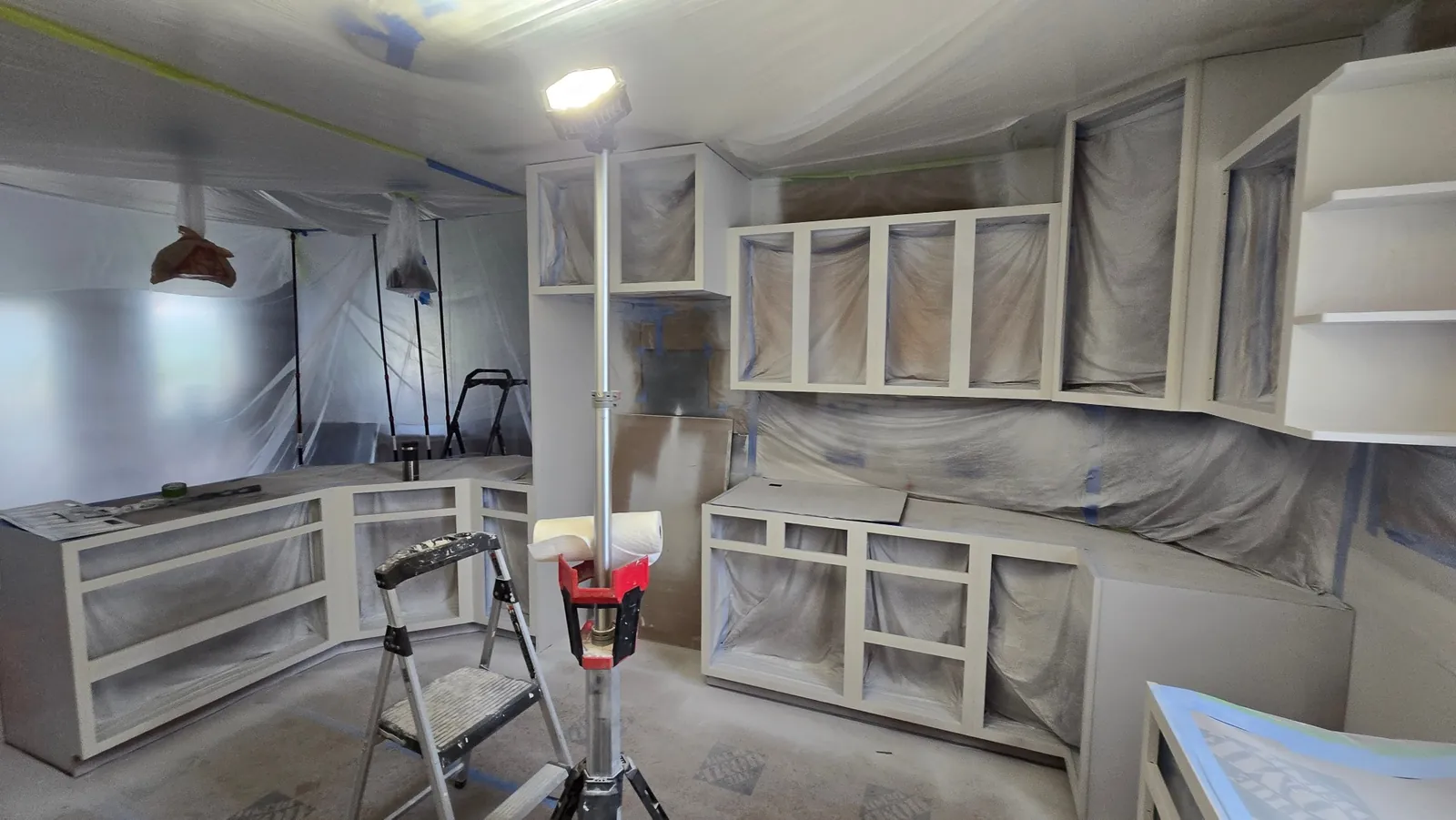 In progress: cabinet frames painted white, doors off, the kitchen masked in plastic