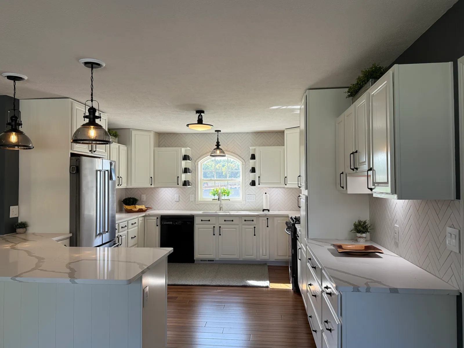 The finished farmhouse kitchen: white painted cabinets and a white herringbone backsplash around the arched window