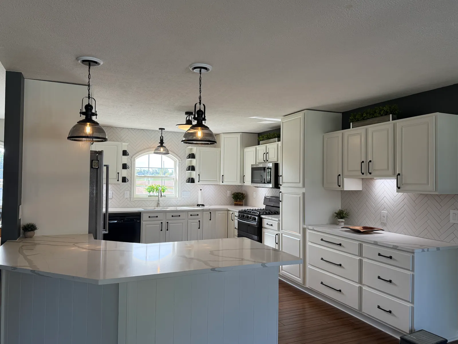 Finished: white cabinets with black pulls and herringbone tile along the range wall