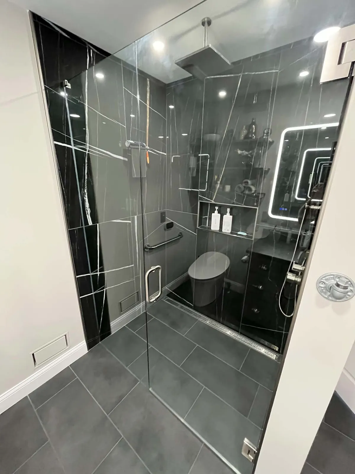 Finished: slab-look black porcelain shower with frameless glass and LED mirror