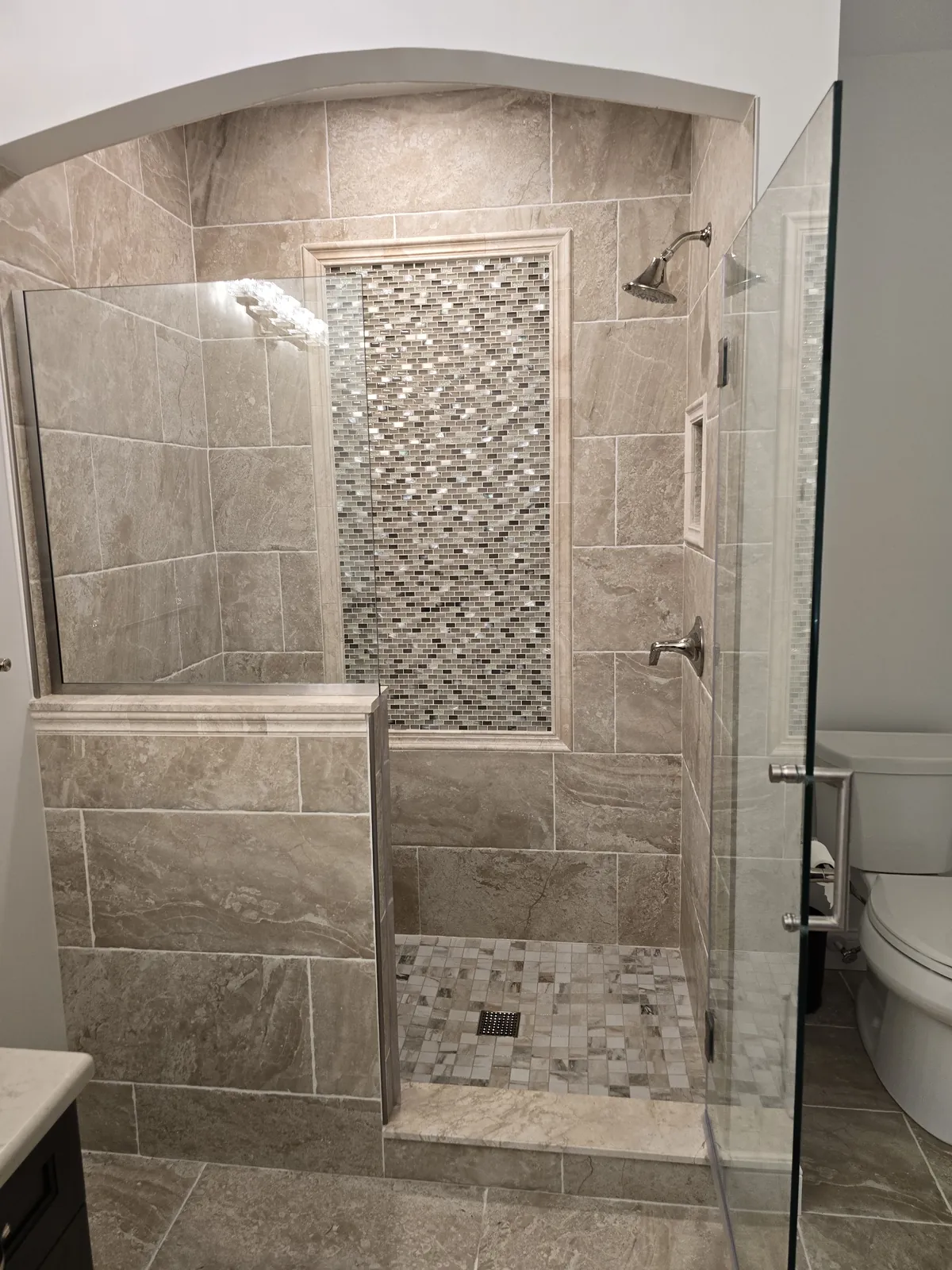 The finished arched shower with glass panel and marble-look tile