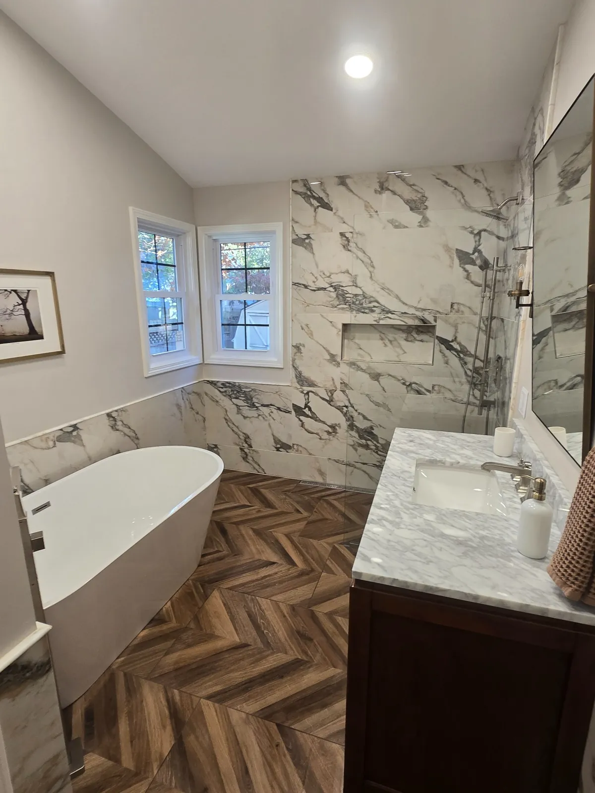 The finished West Bloomfield primary bath: freestanding tub, marble walls and herringbone floor